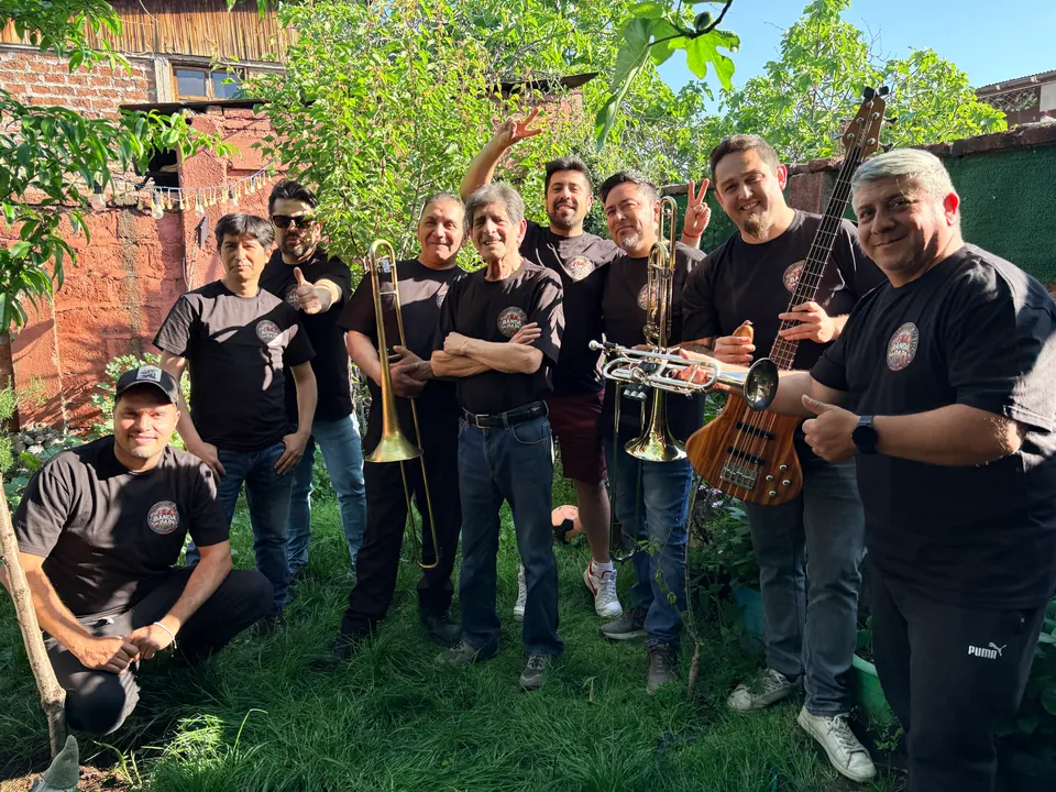Los músicos de La Banda del Papi con poleras negras e instrumentos, en una foto grupal en un jardín