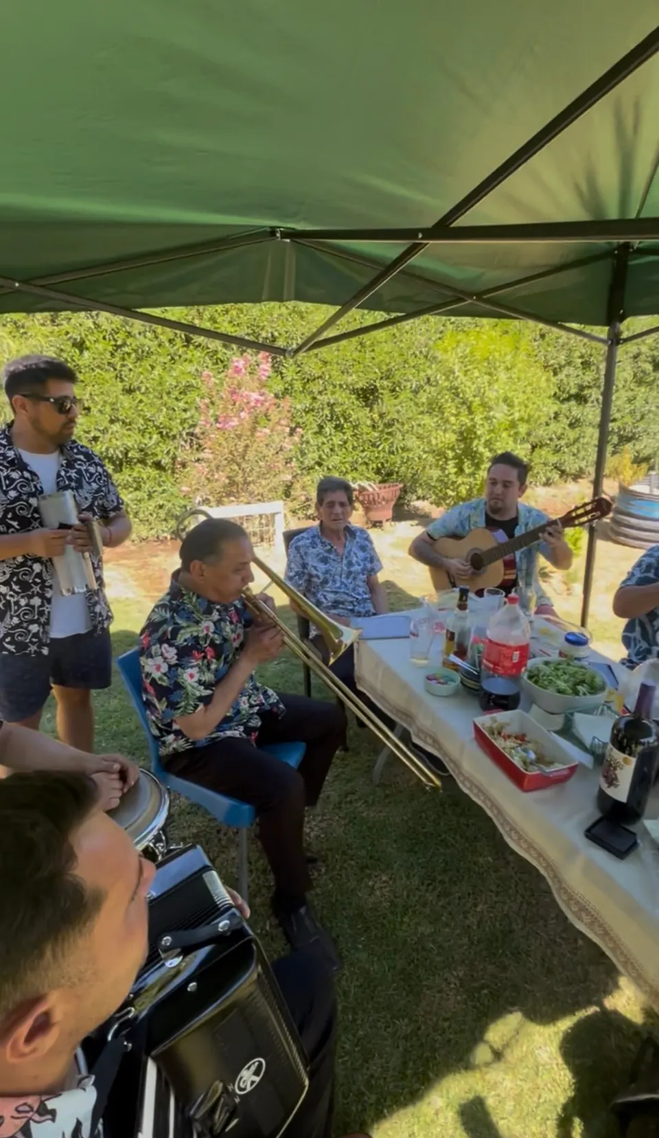 Ensayo de La Banda del Papi bajo un toldo en el patio, entre los instrumentos y la mesa servida