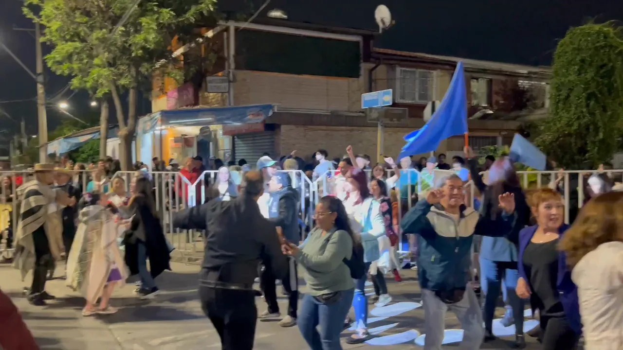 Público celebrando con banderas en la calle frente al escenario, al atardecer